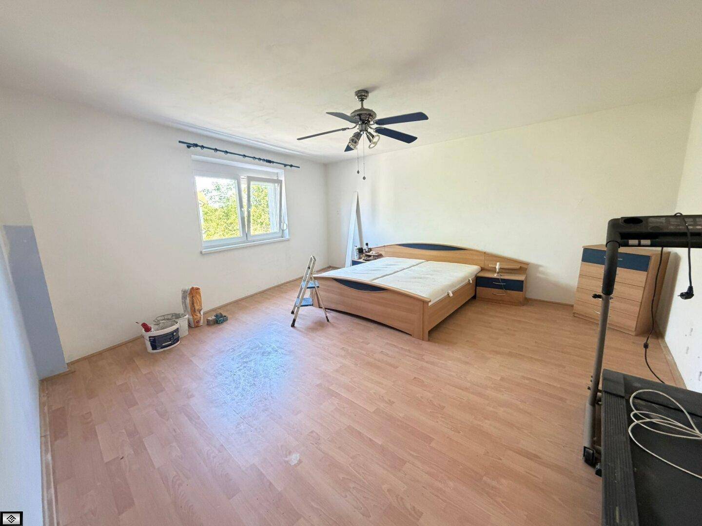 Schlafzimmer mit Doppelbett, Deckenventilator, Laminatboden und einem großen Fenster.