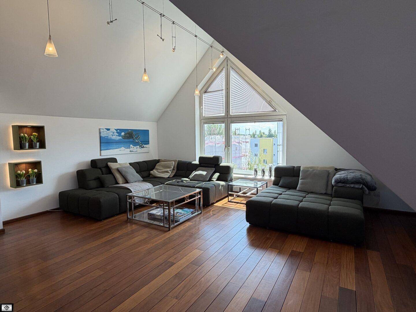 Großzügiges Wohnzimmer mit dunklem Ecksofa, Holzboden und beeindruckendem Giebelfenster.