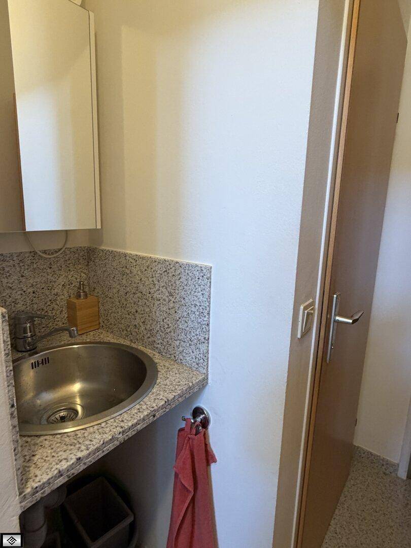 Gäste-WC mit Waschbecken, Spiegelschrank und gefliestem Bereich in hellem Granit-Look.