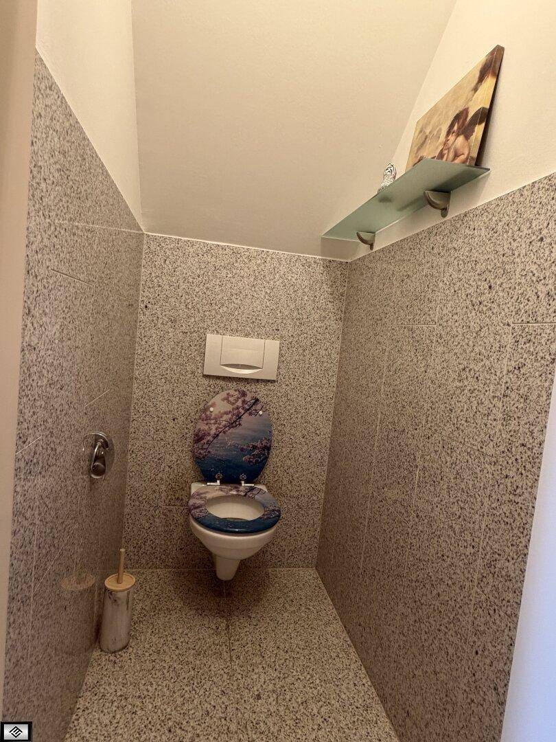 Kleines WC mit wandhängender Toilette und gefliesten Wänden in hellem Granit-Look.