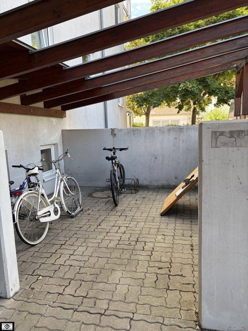 Überdachter Fahrradabstellplatz mit gepflastertem Boden und mehreren Fahrrädern unter einem Holzdach.
