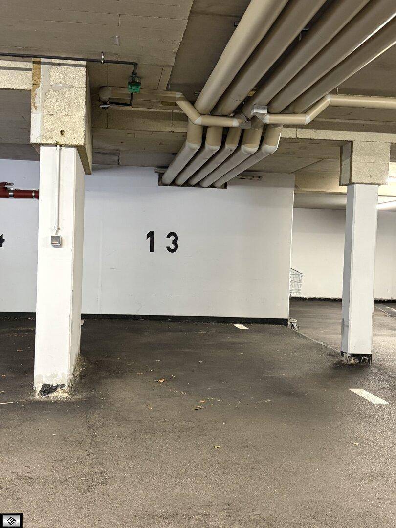Innenansicht einer Tiefgarage mit nummerierten Stellplätzen, Betonstützen und sichtbaren Rohrleitungen.