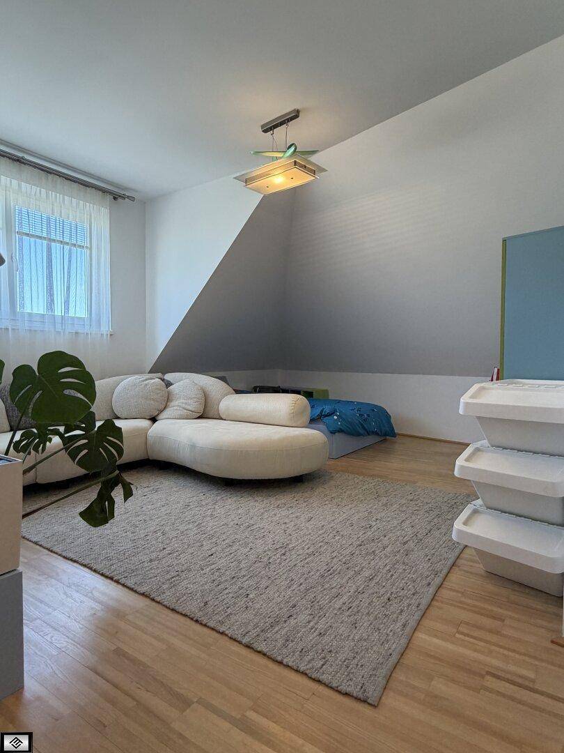 Gemütlicher Wohnbereich mit Dachschräge, weißem Sofa und hellem Holzboden, gut beleuchtet.