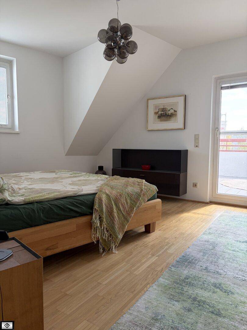 Schlafzimmer mit Holzbett, Dachschräge und Zugang zu einem Außenbereich, hell und freundlich.