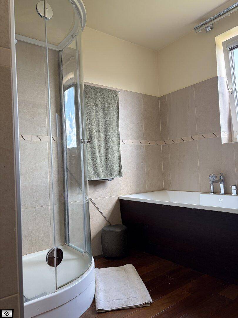 Badezimmer mit Eckdusche und Badewanne, hell gefliest und mit dunklem Holzboden.