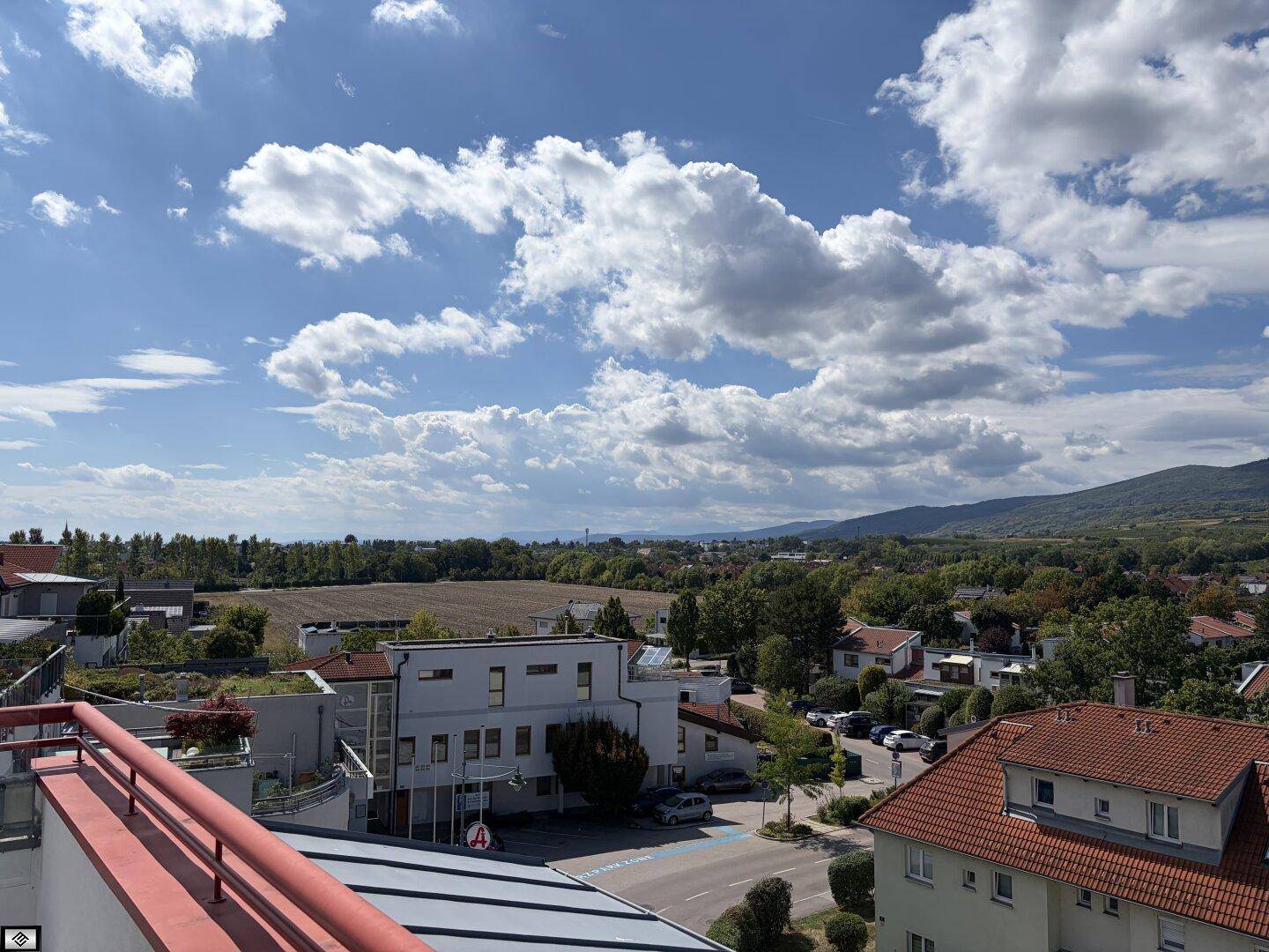 Weitläufiger Blick über eine Stadtlandschaft mit Feldern und Bergen unter einem bewölkten Himmel.