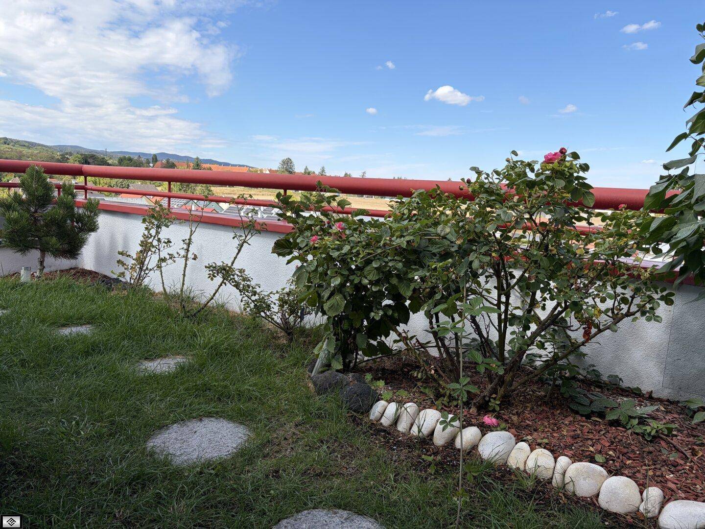 Gepflegter Gartenbereich mit Rosenbüschen und weitem Blick in die Landschaft unter blauem Himmel.