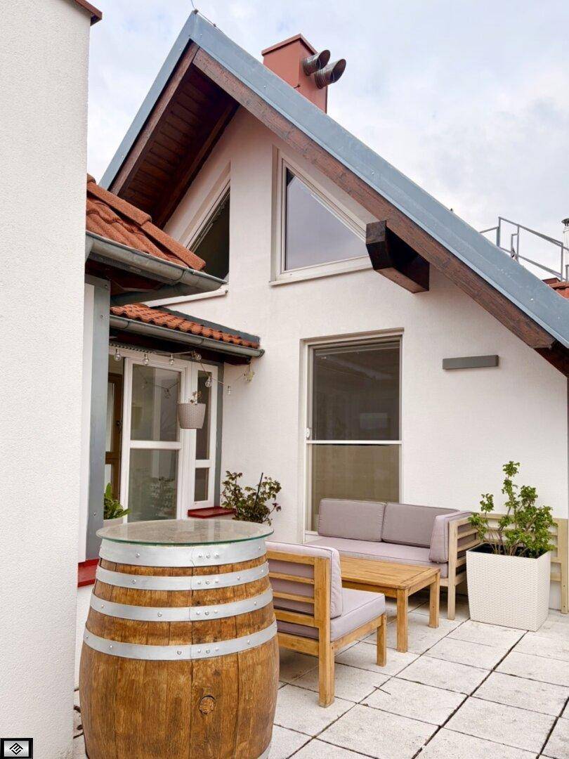 Gemütliche Terrasse mit modernen Gartenmöbeln und einem dekorativen Fass vor der Hausfassade.