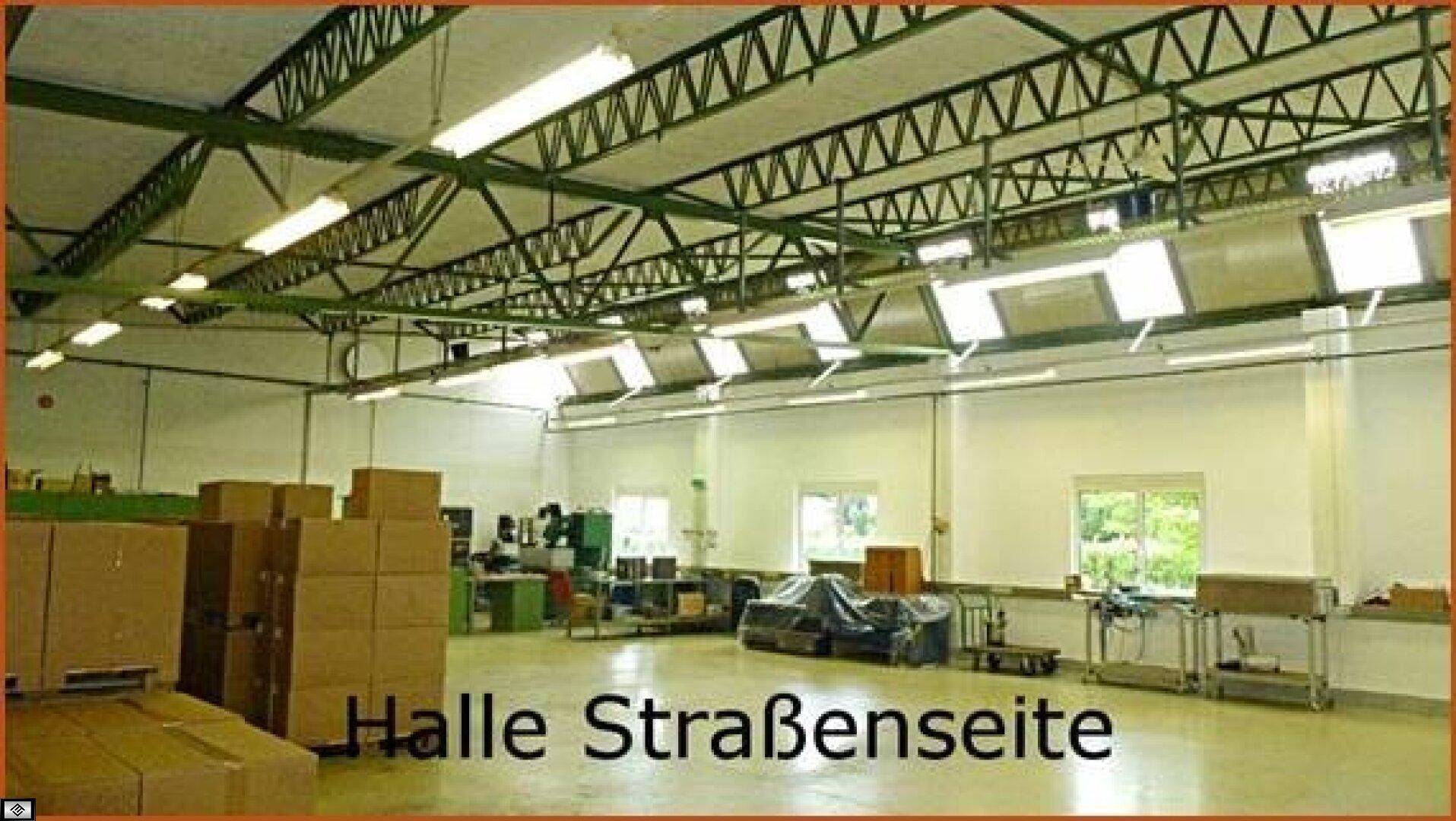 Große Halle mit sichtbaren Dachbindern, Leuchtstoffröhren und einigen Kartons, Blick zur Straßenseite.