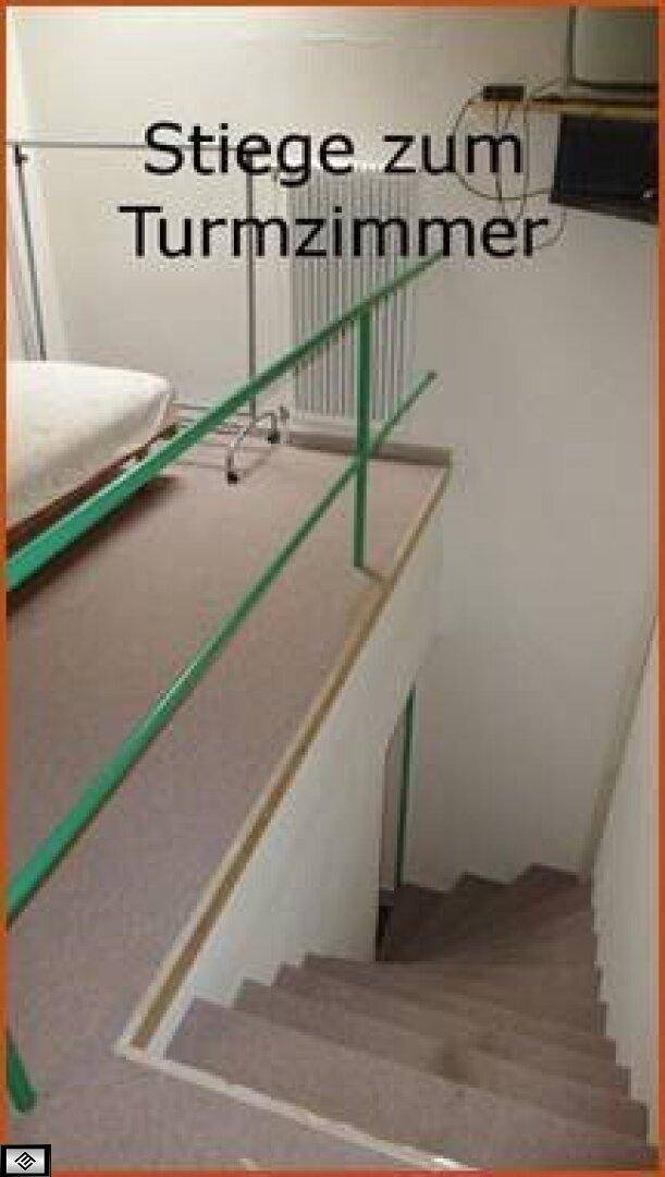 Treppenaufgang mit grünem Geländer, der zu einem oberen Bereich oder Turmzimmer führt.