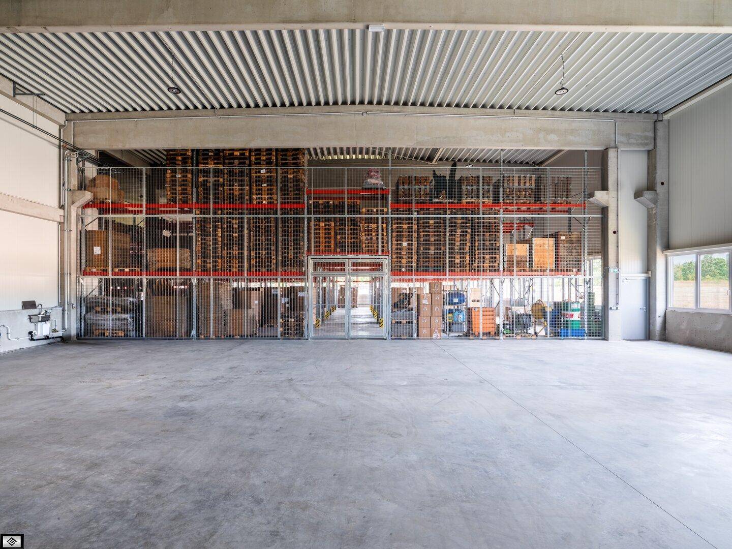 Lagerhalle mit hohen Regalen, gefüllt mit Paletten und Kartons, sowie einem breiten Gang.