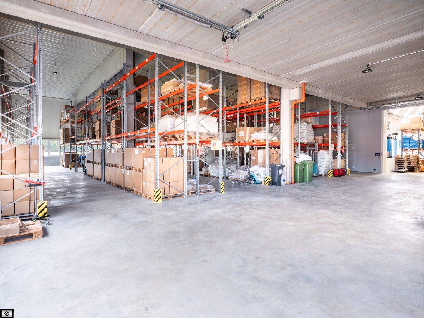 Große Lagerhalle mit umfangreichen Regalsystemen, gefüllt mit verschiedenen Gütern und viel Freifläche.