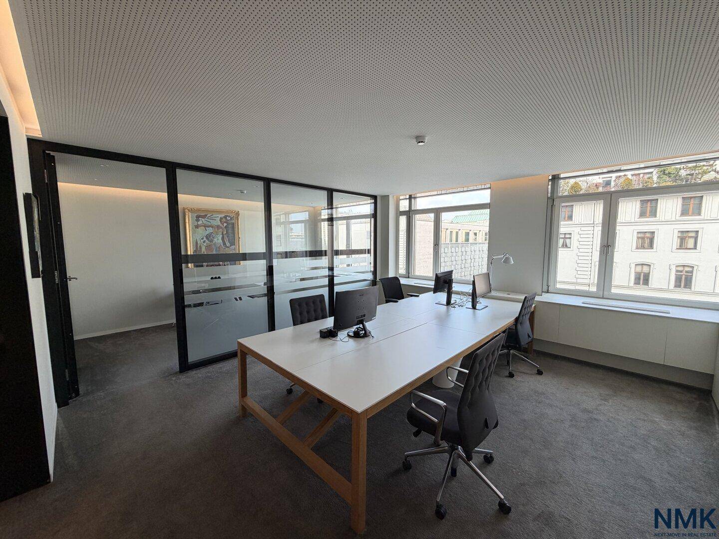 Helles Büro mit großem Tisch, mehreren Arbeitsplätzen und Blick auf die Stadt durch große Fenster.