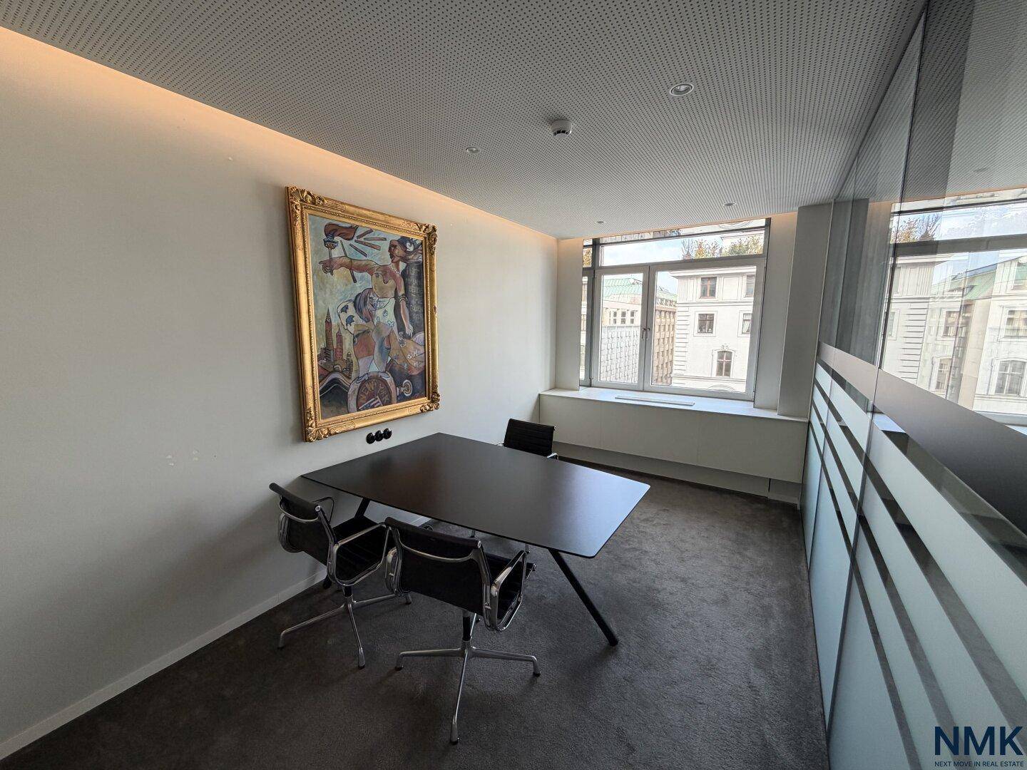 Kleiner Besprechungsraum mit schwarzem Tisch, Stühlen und einem großen Kunstwerk an der Wand.