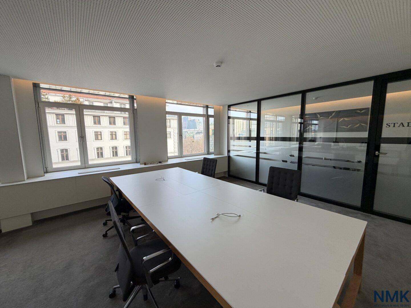 Großer Besprechungsraum mit langem weißen Tisch, bequemen Stühlen und Blick auf die Stadt.