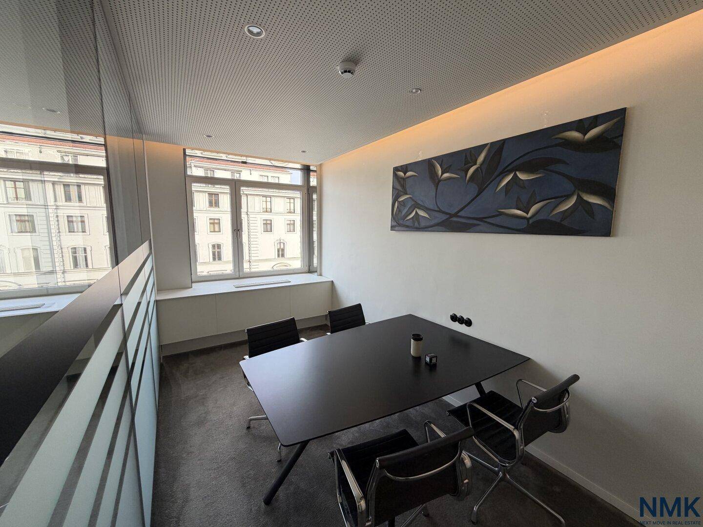 Kleiner, heller Besprechungsraum mit schwarzem Tisch, Stühlen und einem modernen Kunstwerk.