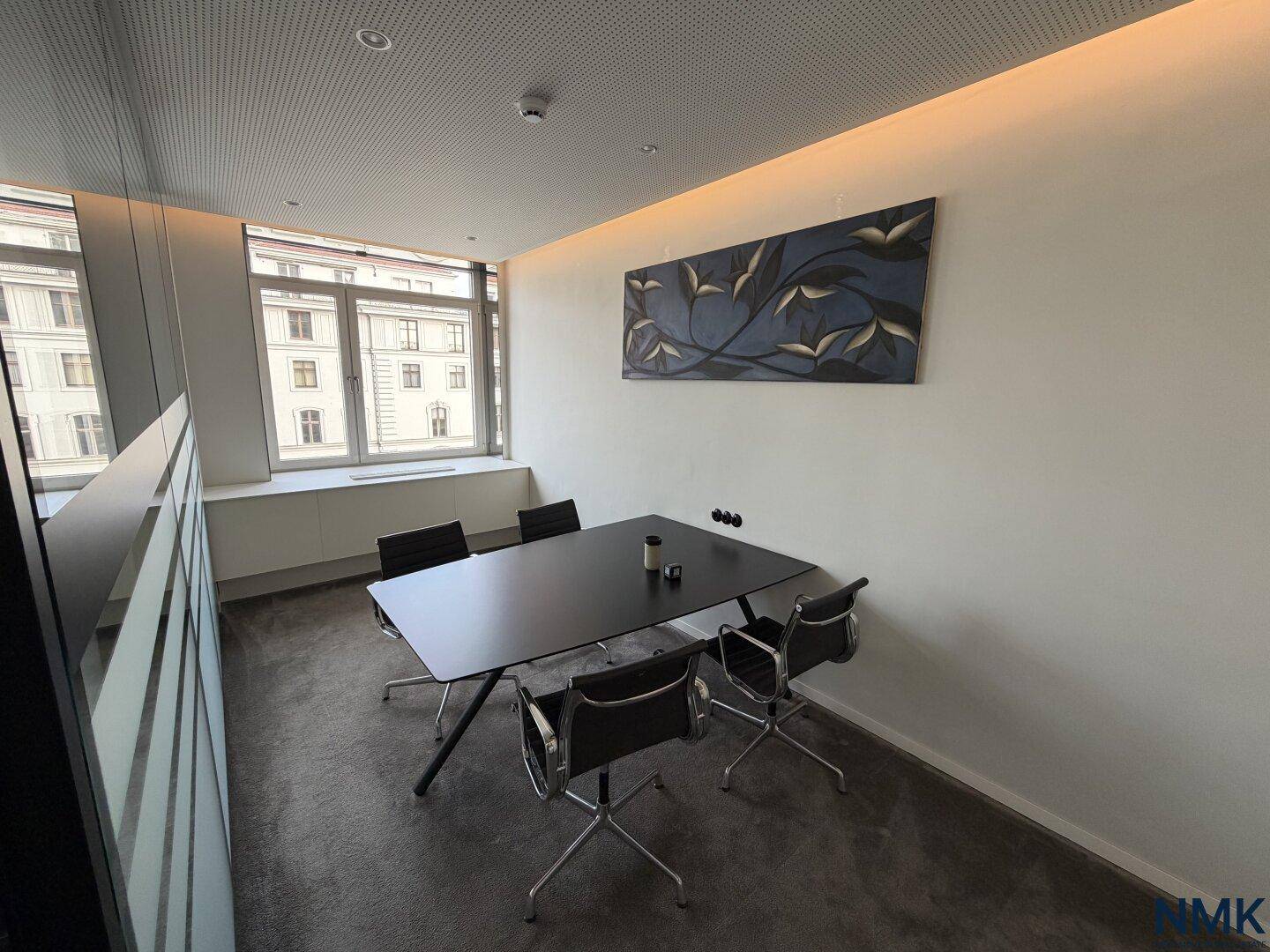 Moderner Besprechungsraum mit großem schwarzen Tisch, Stühlen und einem Fenster mit Tageslicht.