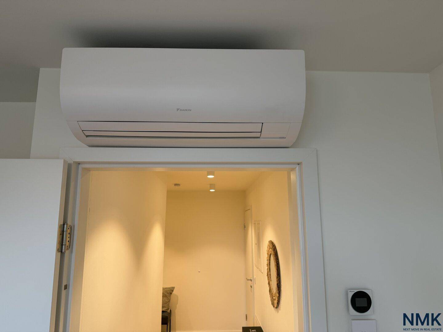 Detailaufnahme einer Klimaanlage über einem Türrahmen in einem hellen Innenraum.