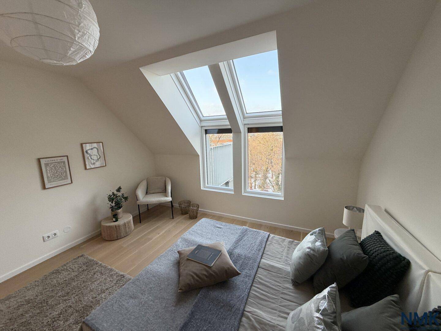 Helles Schlafzimmer im Dachgeschoss mit Holzboden, großem Bett und schrägen Dachfenstern.