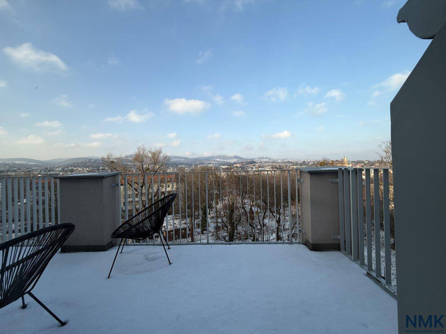 Große, schneebedeckte Terrasse mit Sitzgelegenheiten und weitem Blick über die Stadt und Berge.