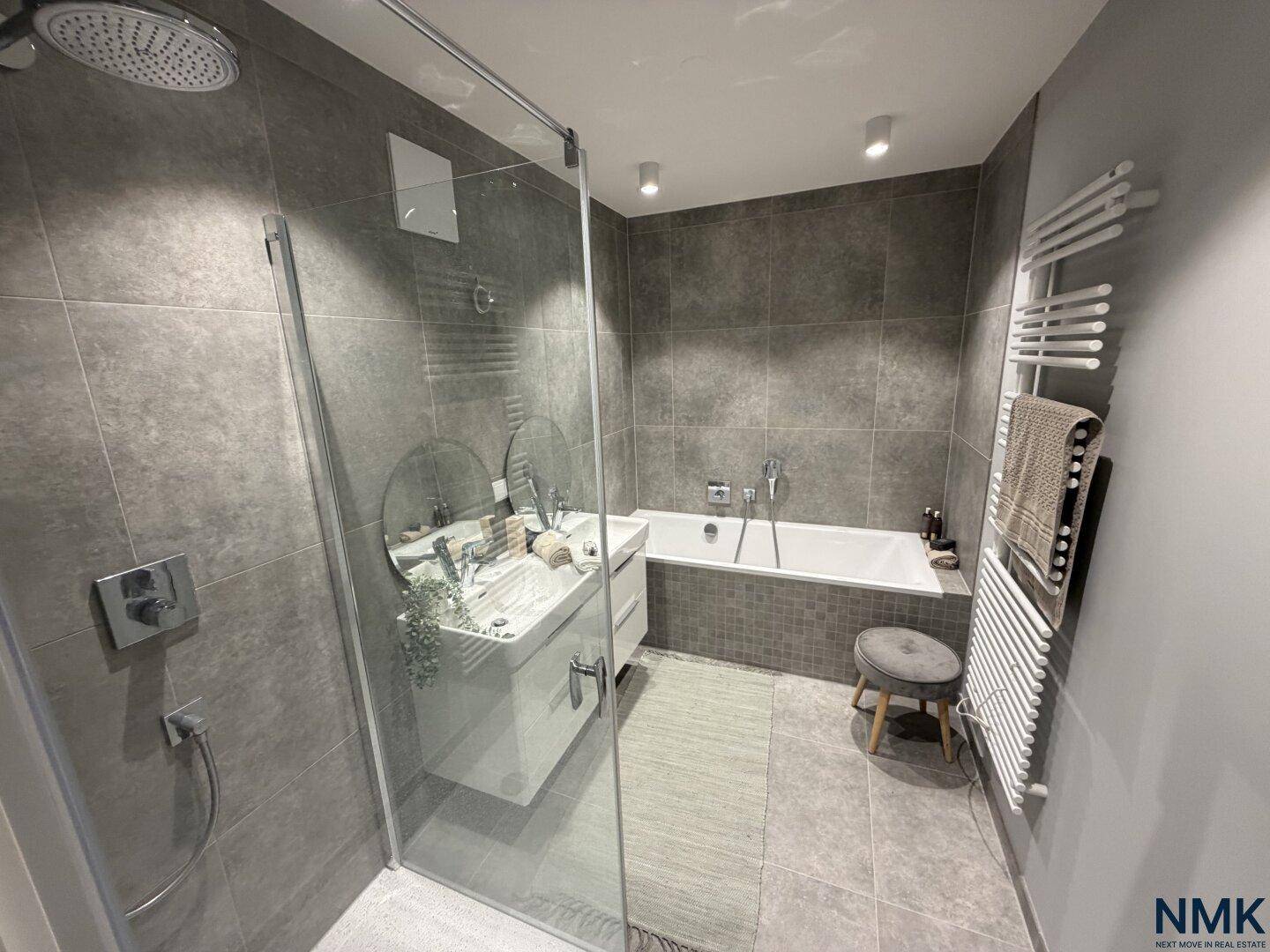 Modernes Badezimmer mit grauen Fliesen, Dusche, Badewanne und beheiztem Handtuchhalter.