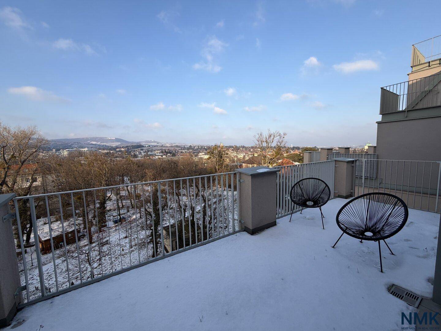Geräumige Terrasse mit Metallgeländer und Blick auf die verschneite Stadt und die Hügel.