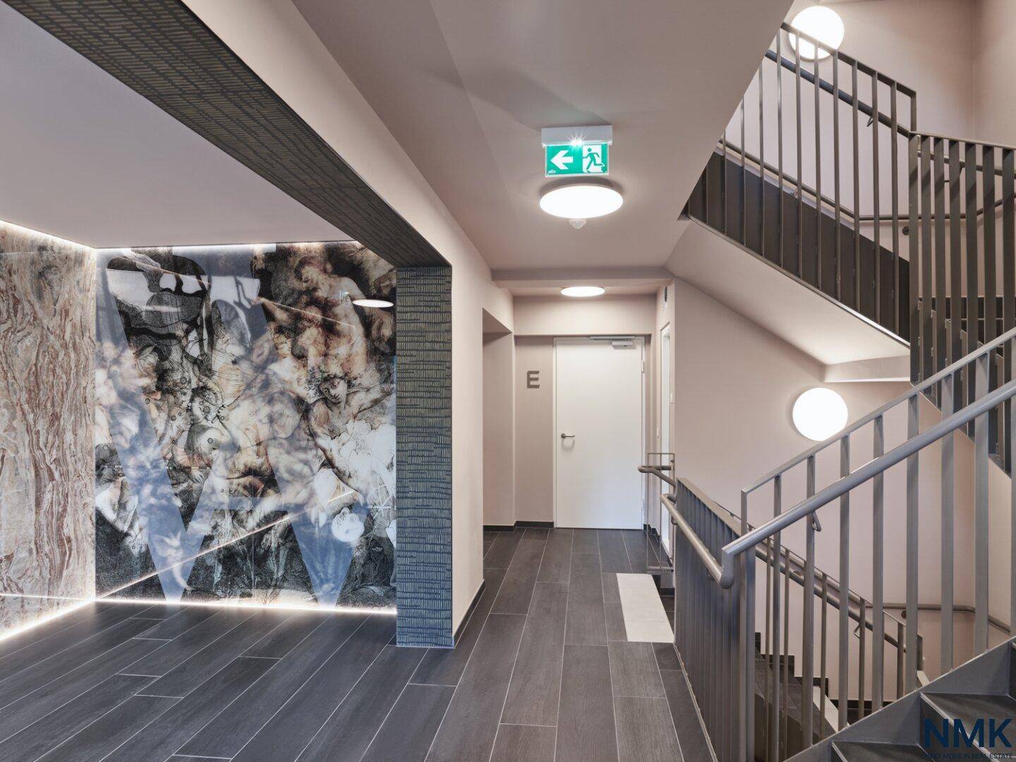 Modern gestalteter Treppenhausbereich mit Fliesenboden, Metallgeländer und dekorativer Wandverkleidung.