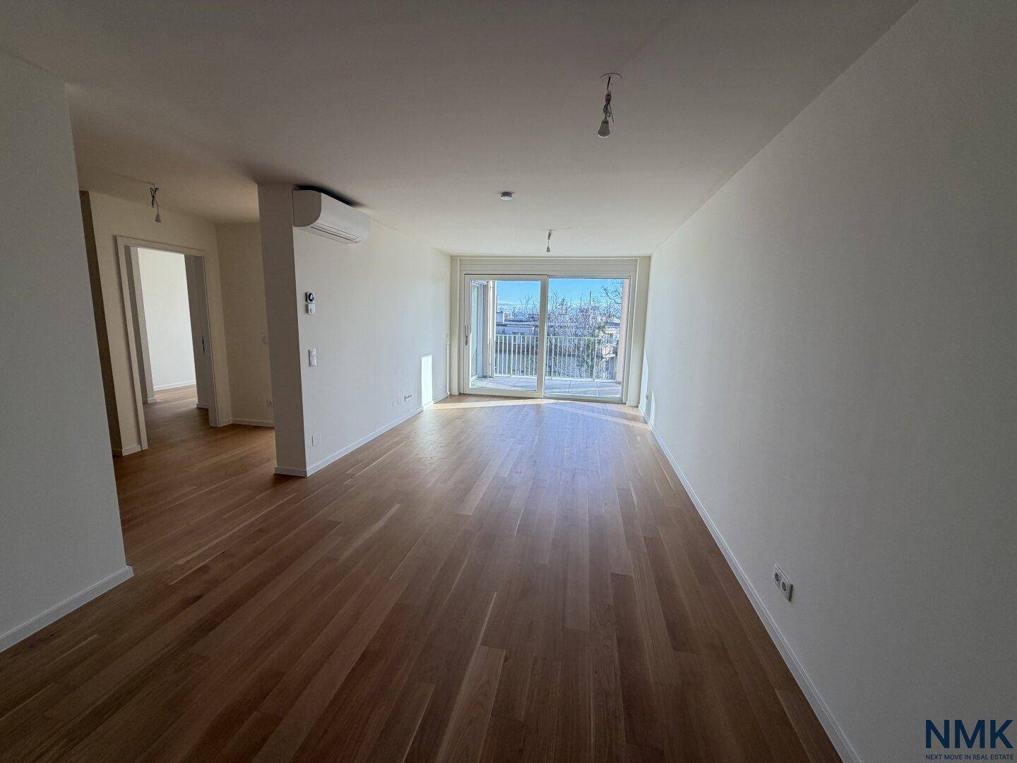 Geräumiges, unmöbliertes Wohnzimmer mit Holzboden und großen Fenstern, die viel Tageslicht hereinlassen.