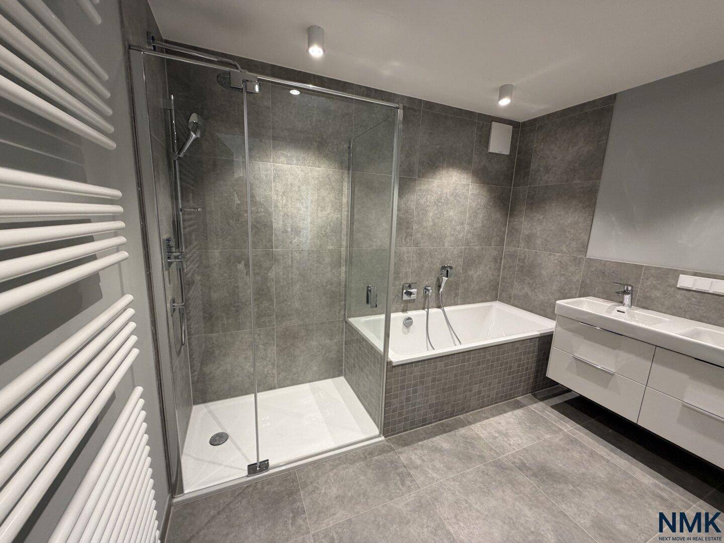 Modernes Badezimmer mit grauen Fliesen, Badewanne, Duschkabine und Doppelwaschbecken.