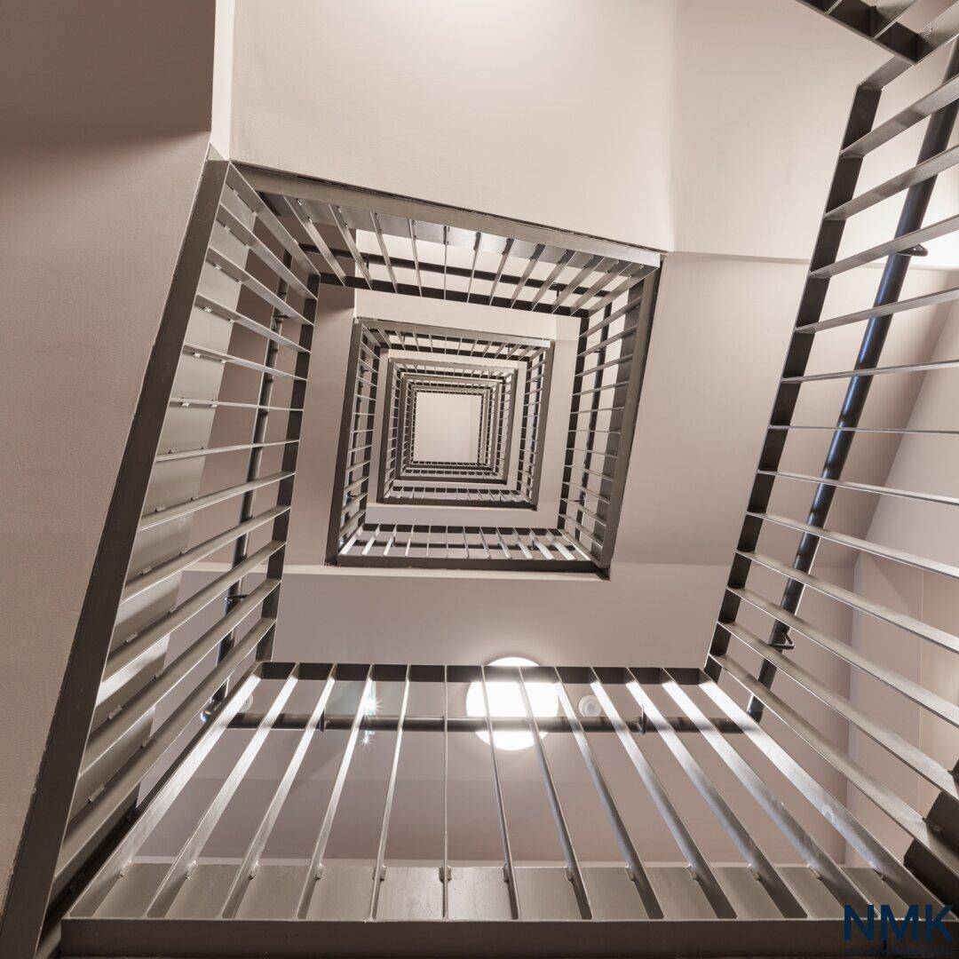 Modernes Treppenhaus mit Metallgeländer und quadratischer Wendeltreppe, von oben fotografiert.