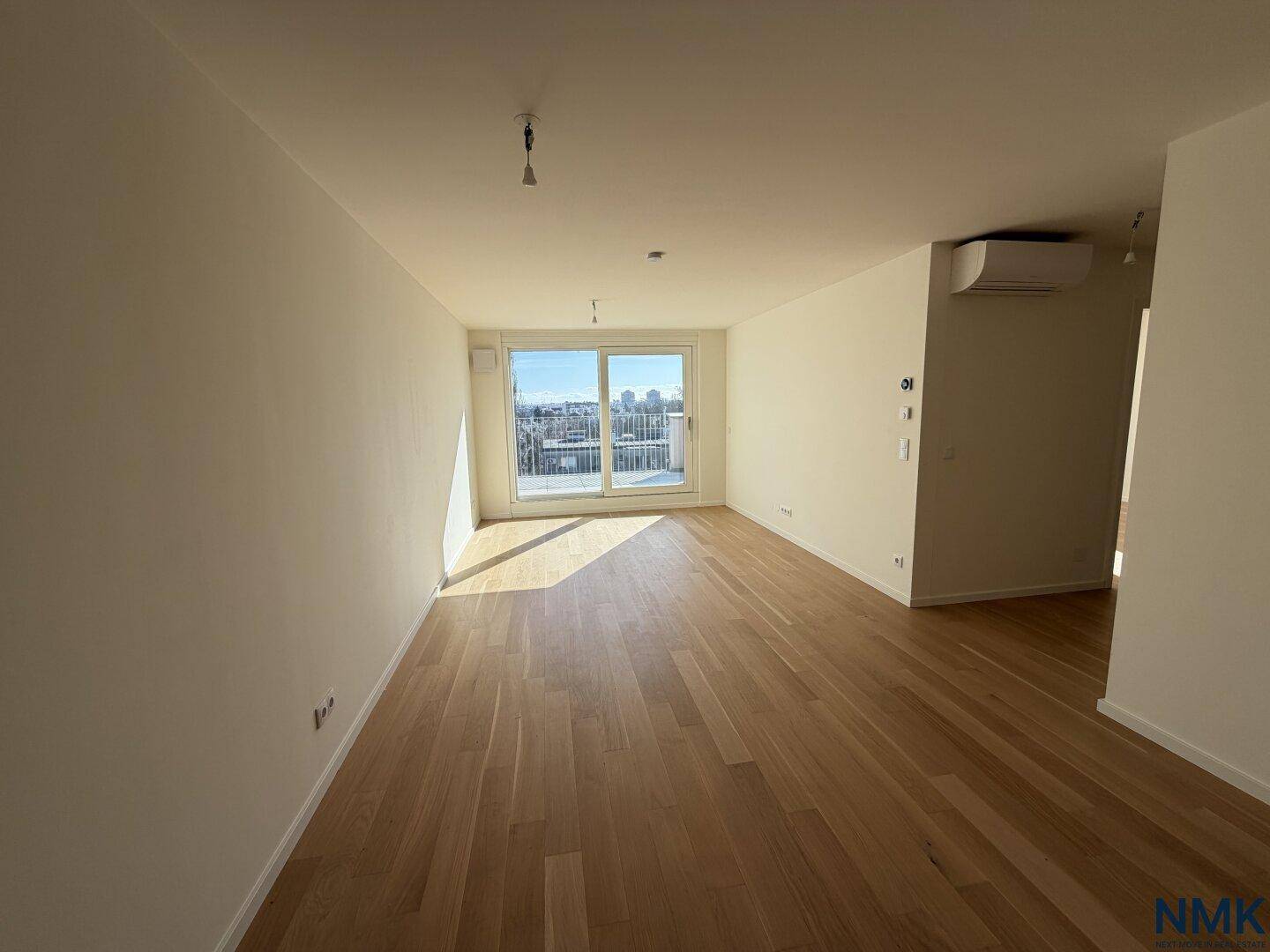 Geräumiges, leeres Wohnzimmer mit Holzboden, Klimaanlage und Zugang zu einem Balkon.