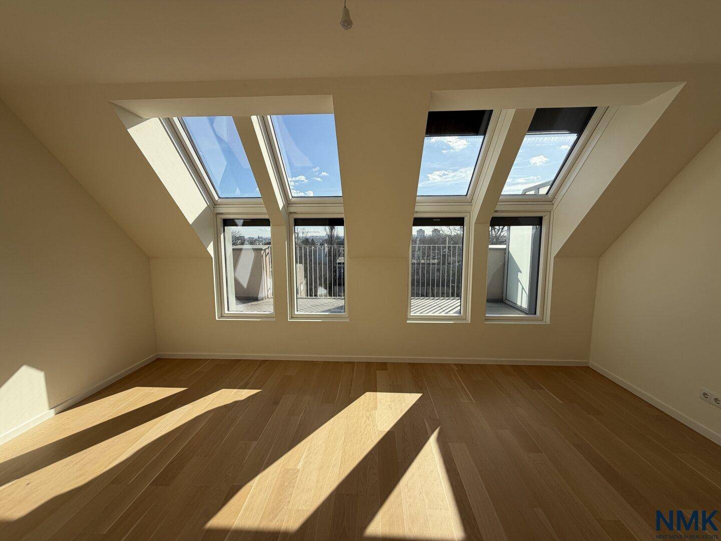 Geräumiges, leeres Schlafzimmer mit Holzboden, Dachschrägen und mehreren Dachfenstern.