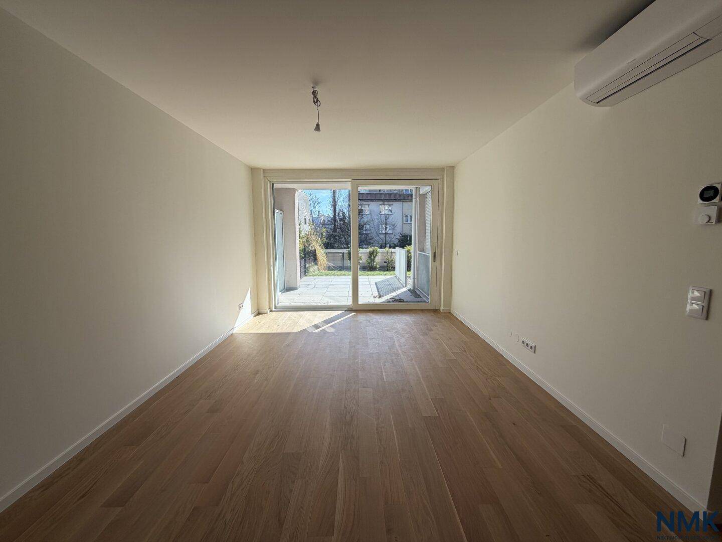 Helles, leeres Wohnzimmer mit Holzboden und großen Schiebetüren zur Terrasse.