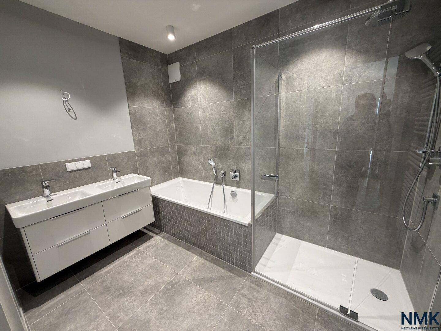 Modernes Badezimmer mit grauen Fliesen, Badewanne und separater Duschkabine.