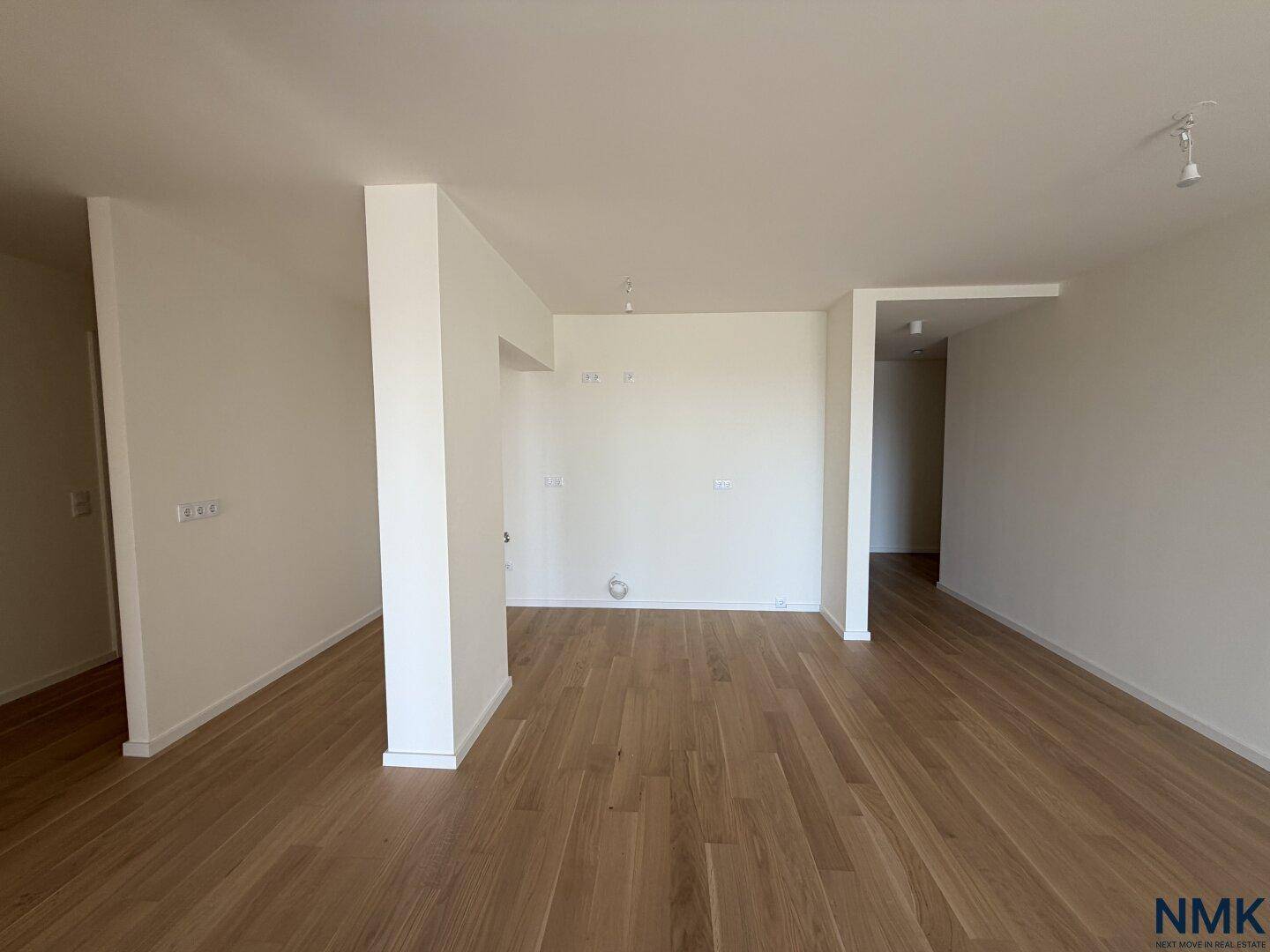 Offener Wohnbereich mit Holzboden, vorbereitet für die Kücheninstallation.