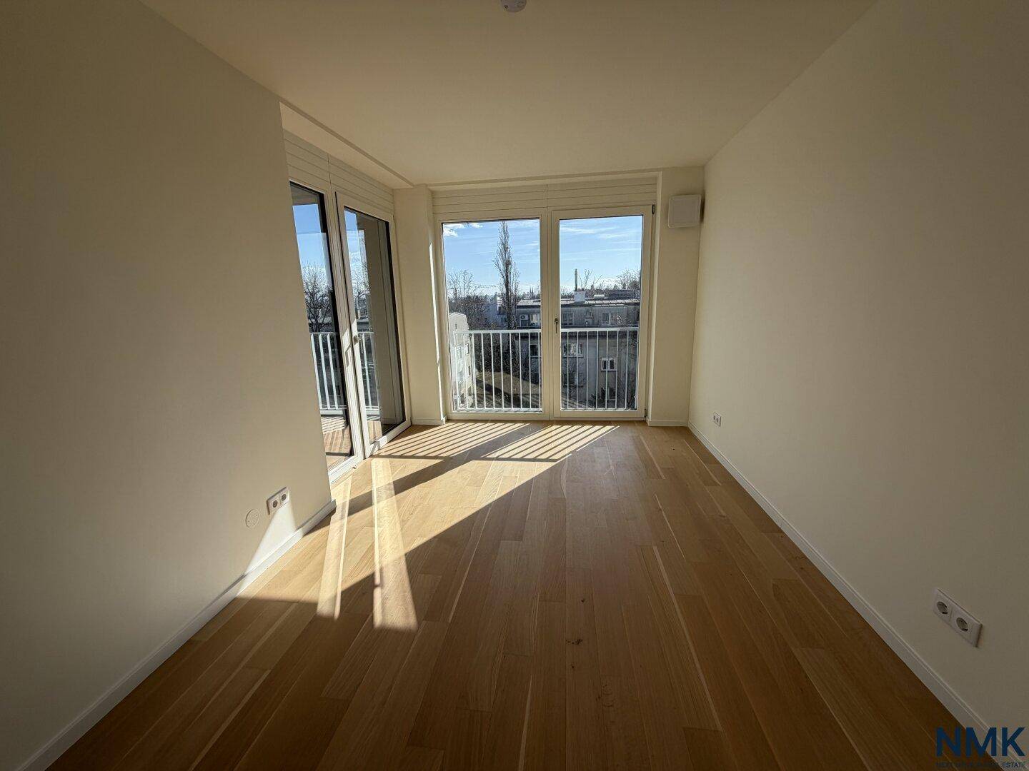Helles Zimmer mit Holzboden und Zugang zu einem französischen Balkon.