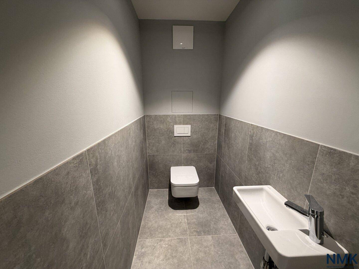 Modernes Gäste-WC mit Wand-WC, kleinem Waschbecken und grauen Fliesen.