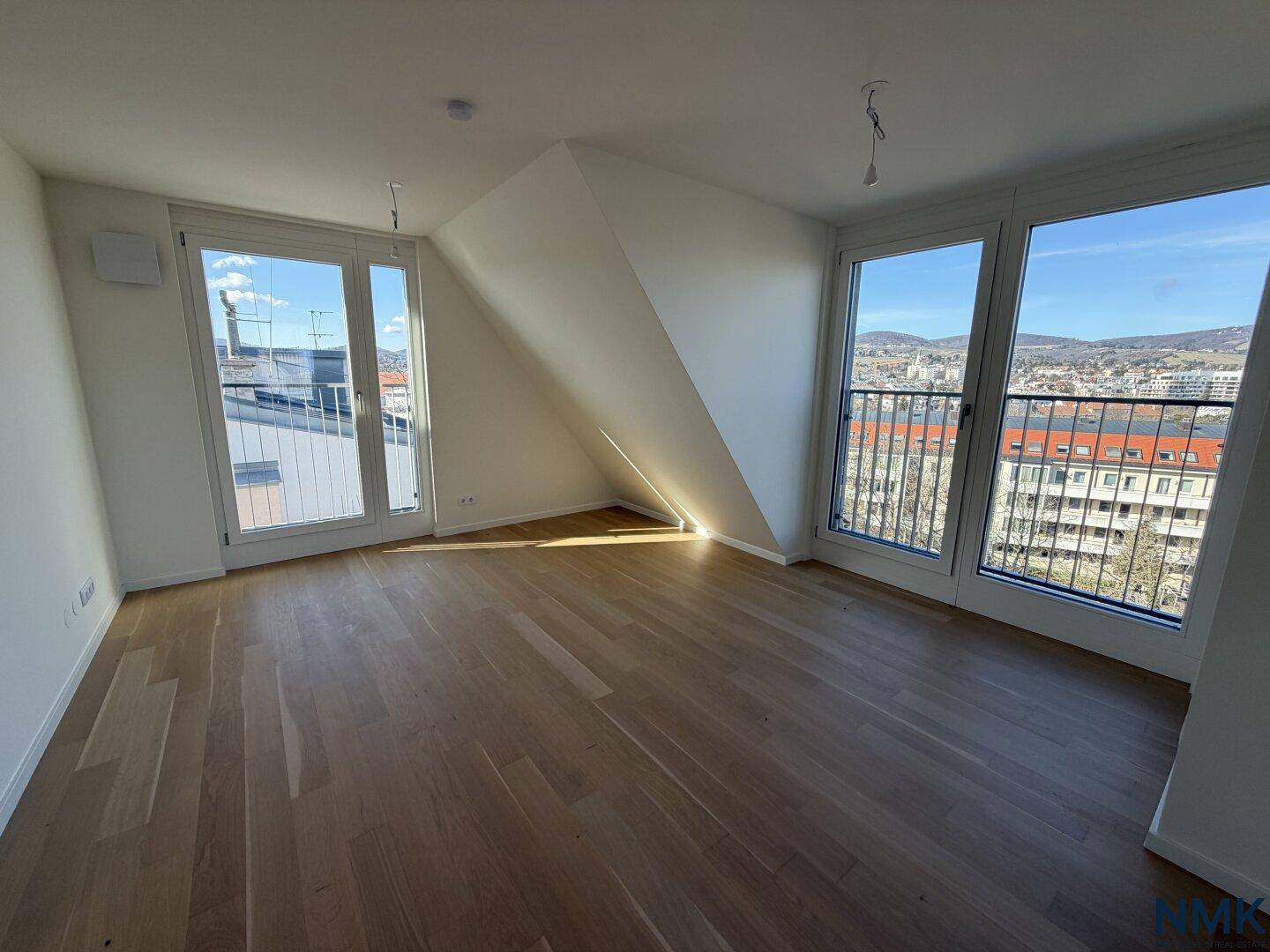 Geräumiger, leerer Raum mit Holzboden, großen Fenstern und viel Tageslicht.