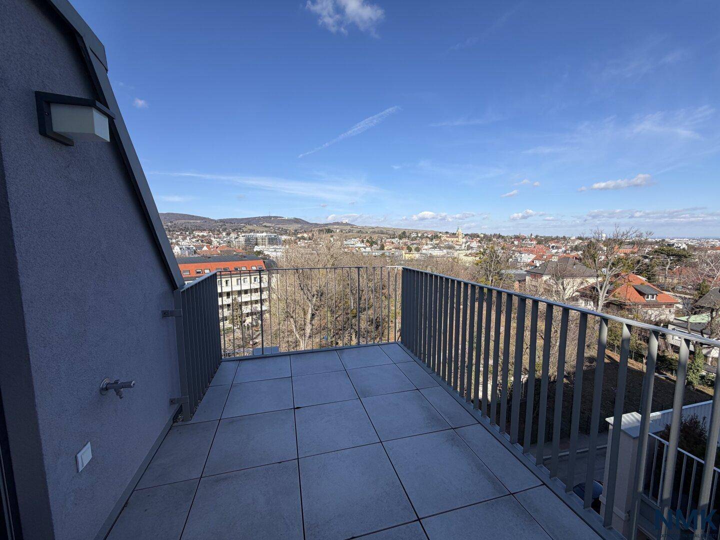 Großer, unmöblierter Balkon mit Fliesenboden und weitem Blick über die Stadt und Berge.