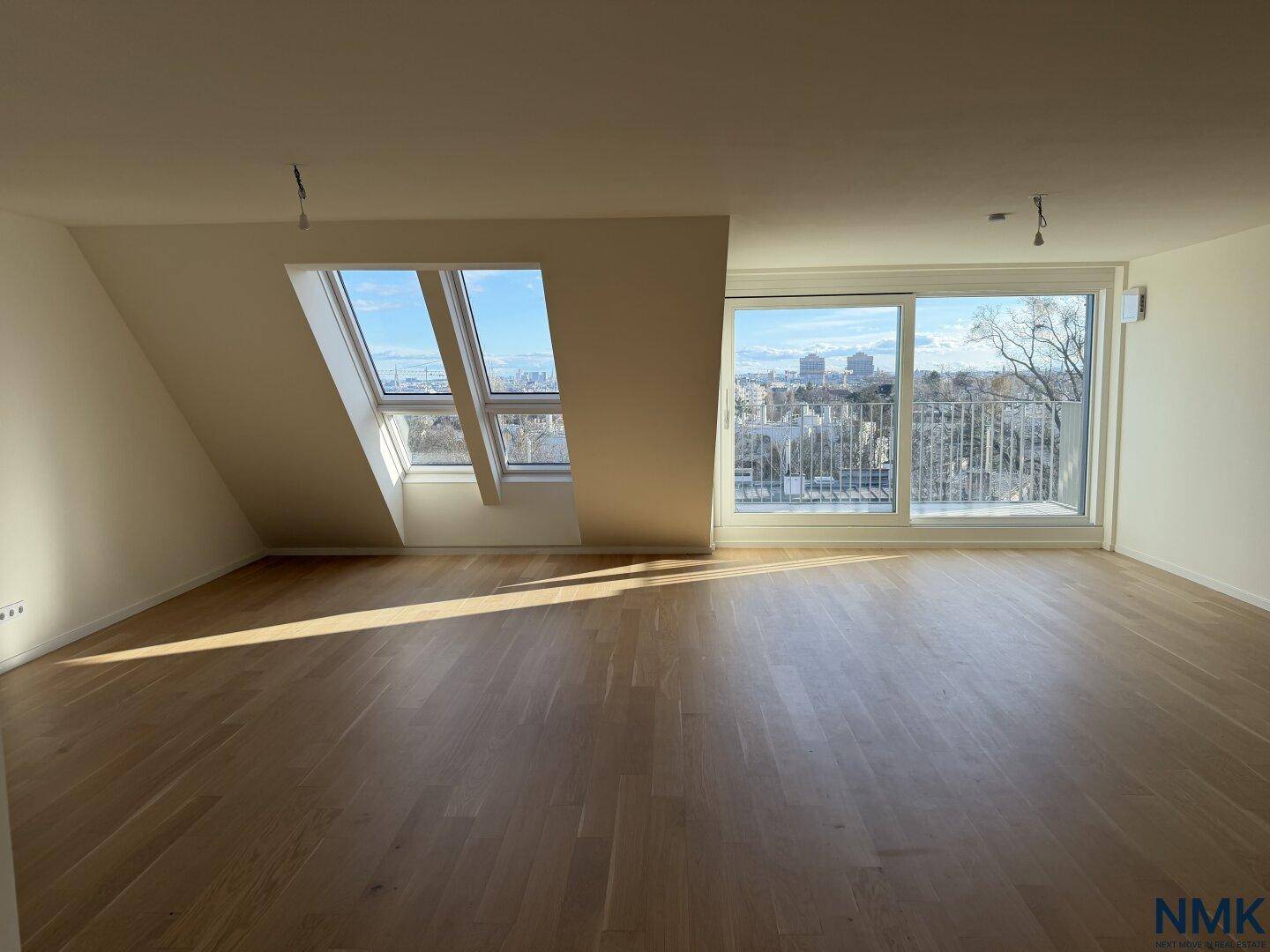 Geräumiger, leerer Wohnbereich mit Holzboden, großen Fenstern und schöner Aussicht auf die Stadt.