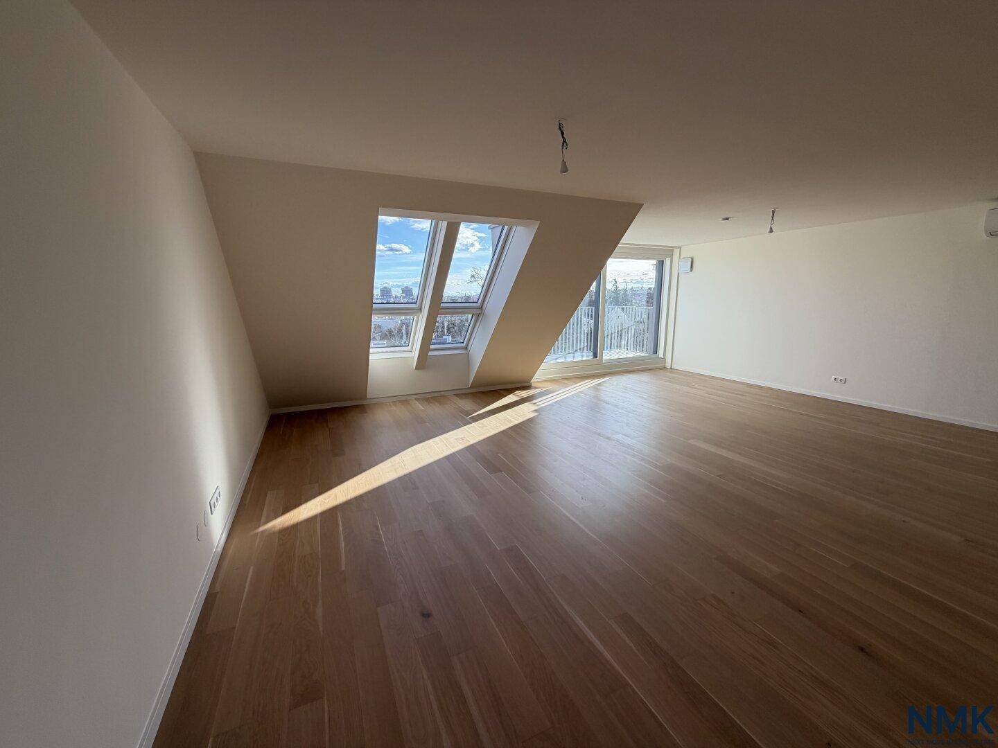 Heller, leerer Wohnraum mit Holzboden, Dachfenstern und Panoramablick über die Stadt.