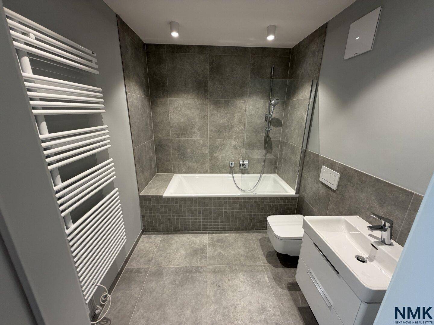 Modernes Badezimmer mit Badewanne, WC, Einzelwaschbecken und beheiztem Handtuchhalter.