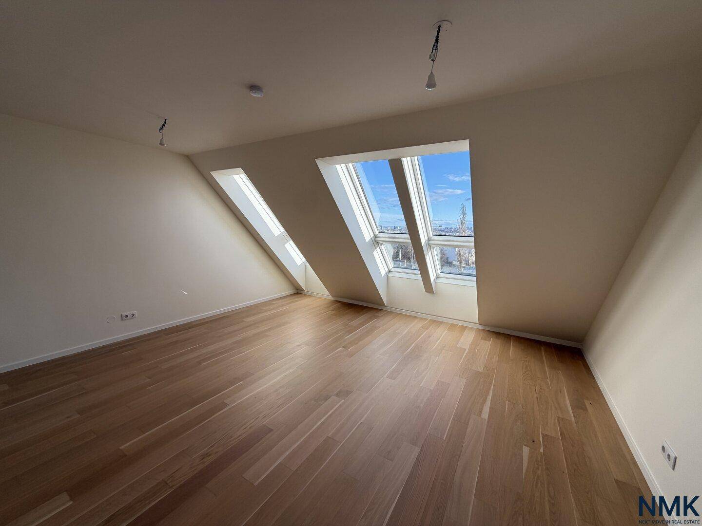 Heller Raum mit Holzboden und mehreren Dachfenstern, die einen weiten Stadtblick bieten.