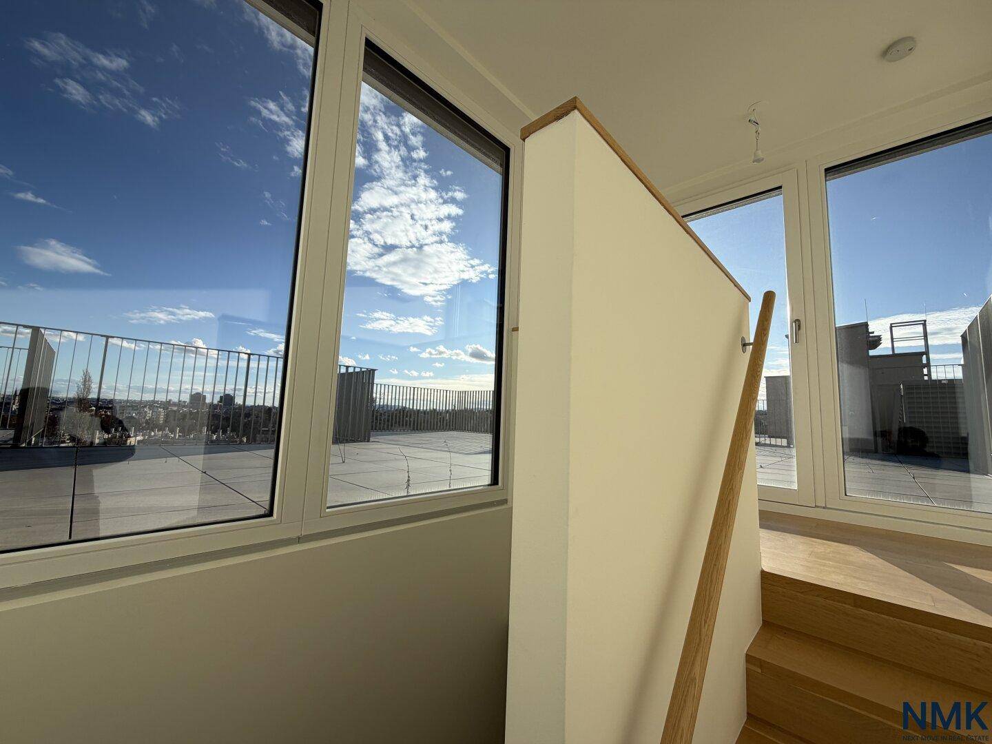 Treppenaufgang zur Dachterrasse mit großen Fenstern und Blick auf die Stadt.