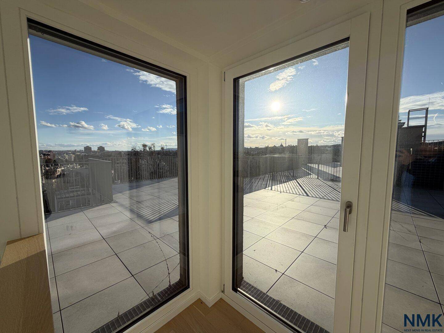 Heller Raum mit großen Fenstern und direktem Zugang zu einer Dachterrasse mit Stadtblick.