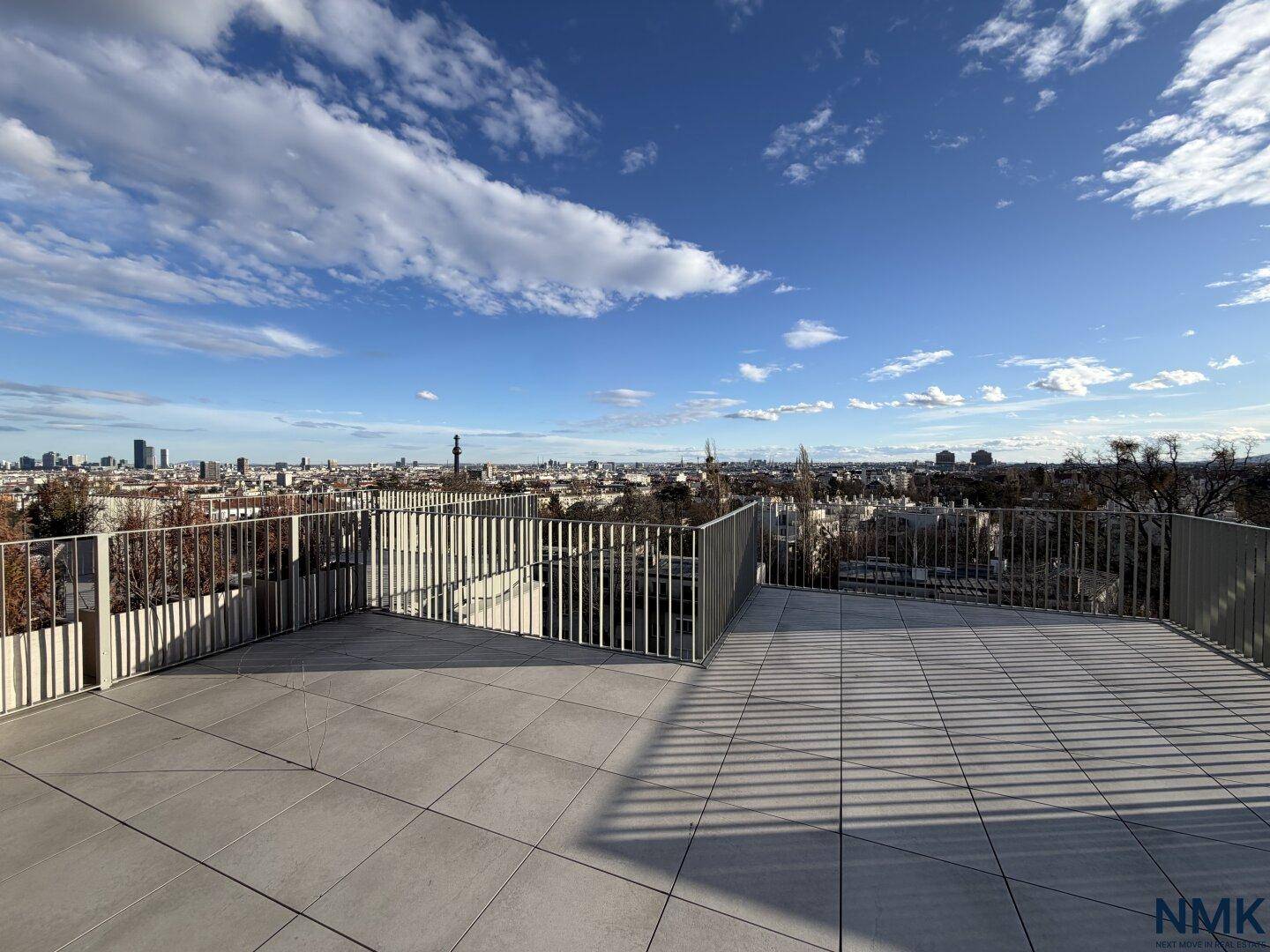 Weitläufige Dachterrasse mit Fliesenboden und Geländer, die einen beeindruckenden Stadtblick bietet.