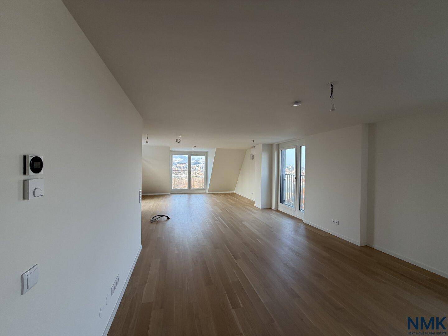 Geräumiger, unmöblierter Wohnbereich mit Holzboden und Zugang zu einem Balkon.