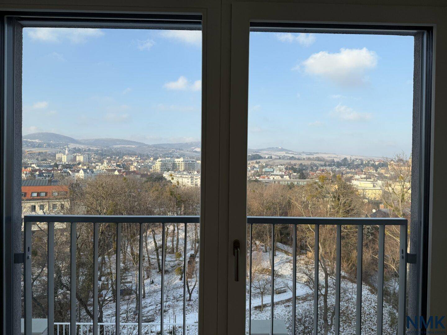 Blick aus dem Fenster auf eine verschneite Stadtlandschaft mit Bergen im Hintergrund.