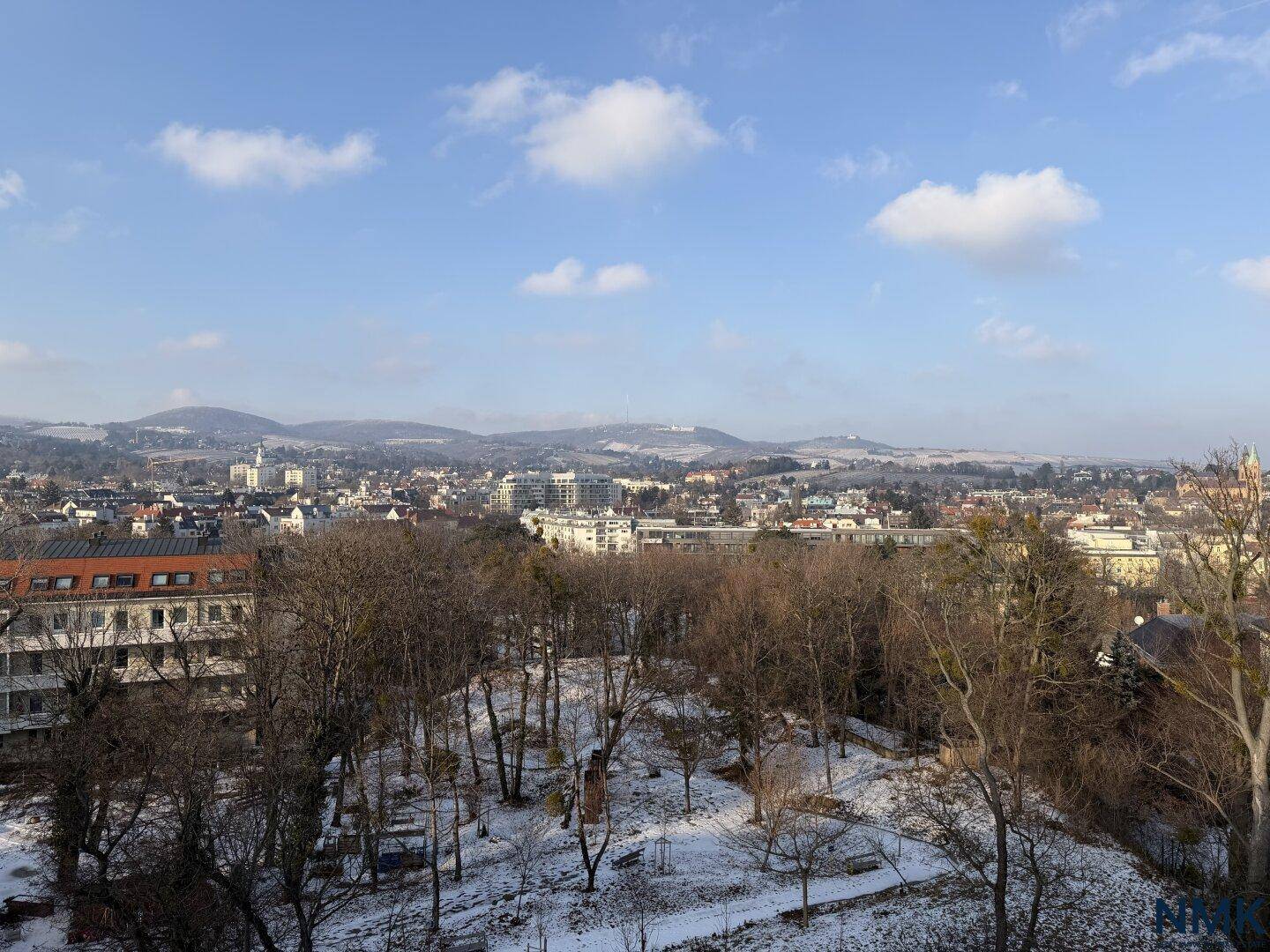 Weitläufiger Blick über eine verschneite Stadt mit bewaldeten Hügeln und Bergen.
