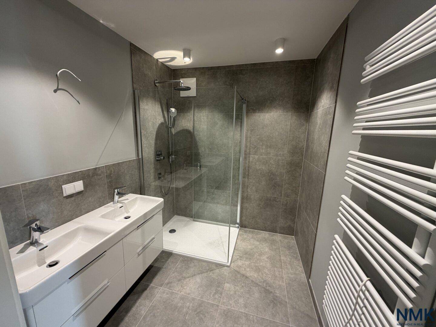 Modernes Badezimmer mit Doppelwaschbecken, großer Dusche und grauen Fliesen.